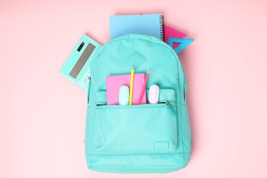 Photo of Backpack with different school stationery on pink background, top view