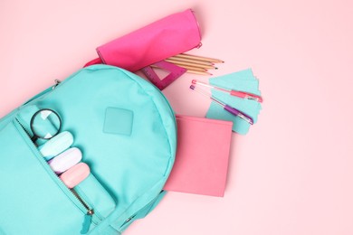 Backpack with different school stationery on pink background, flat lay