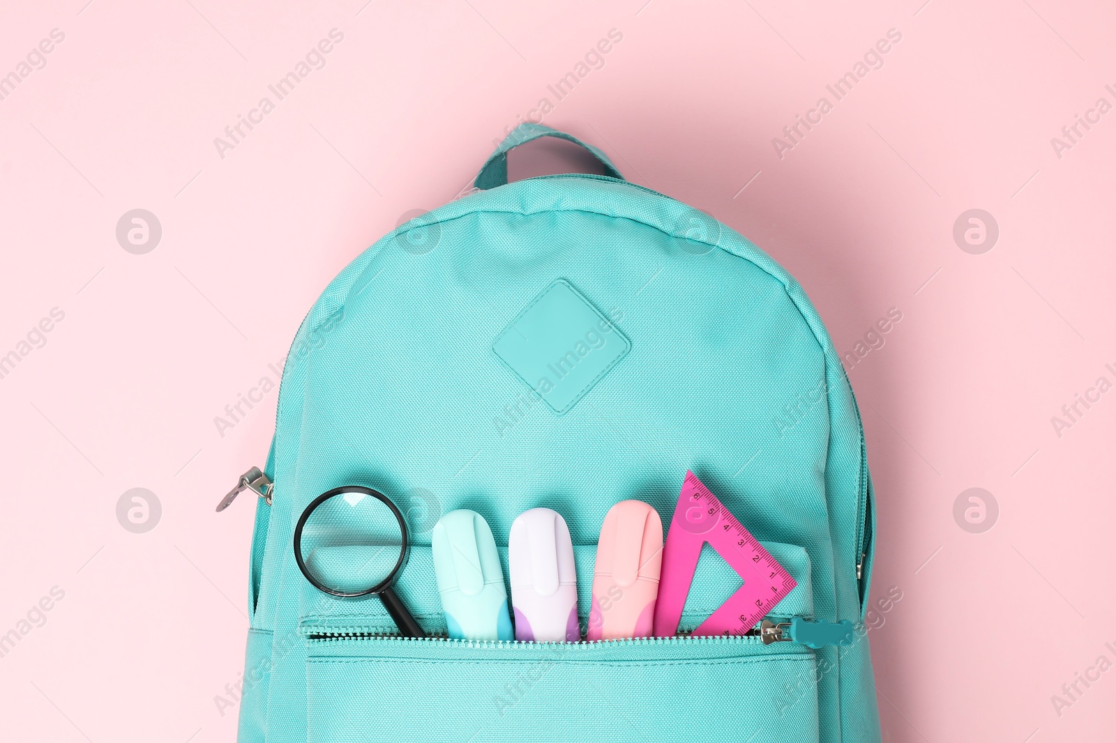 Photo of Backpack with different school stationery on pink background, top view