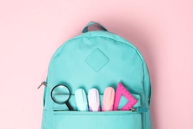 Photo of Backpack with different school stationery on pink background, top view