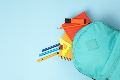 Backpack with different school stationery on light blue background, flat lay. Space for text