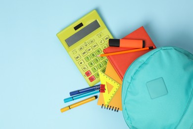 Photo of Backpack with different school stationery on light blue background, flat lay