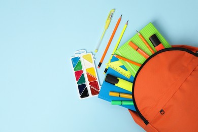 Photo of Orange backpack and different school supplies on light blue background, flat lay. Space for text