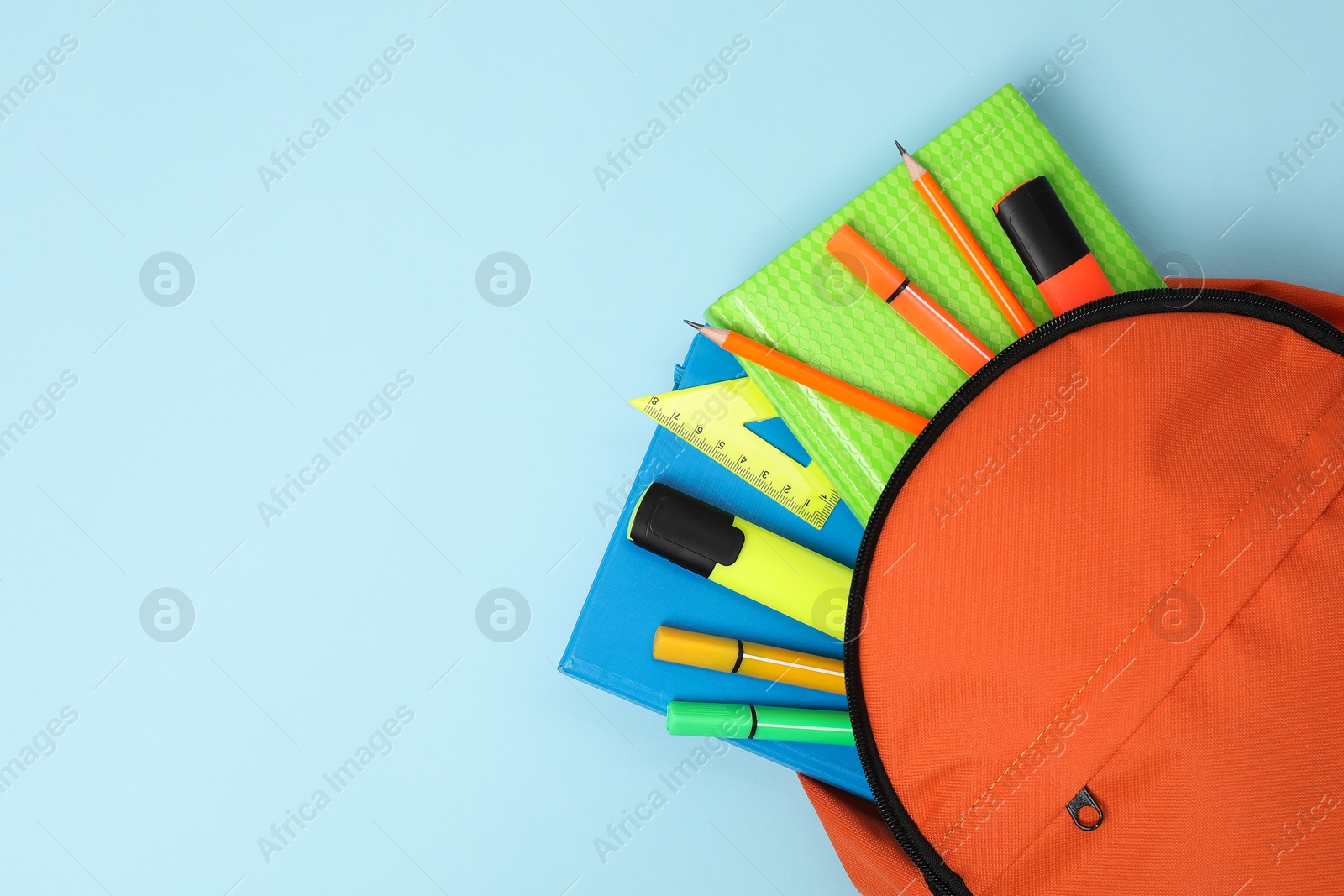 Photo of Orange backpack and different school supplies on light blue background, top view. Space for text