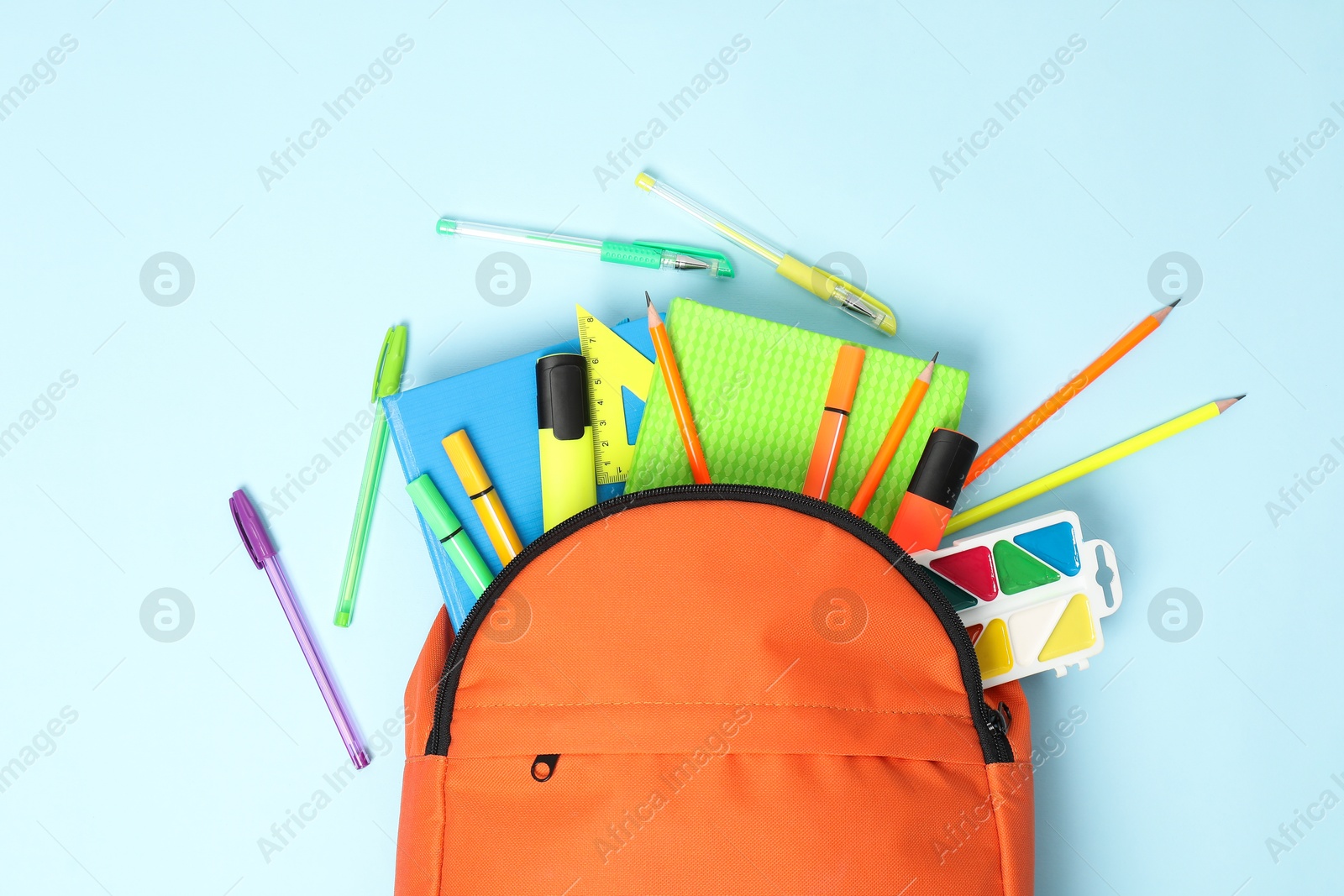 Photo of Orange backpack and different school supplies on light blue background, flat lay