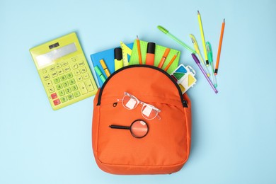 Orange backpack and different school supplies on light blue background, flat lay