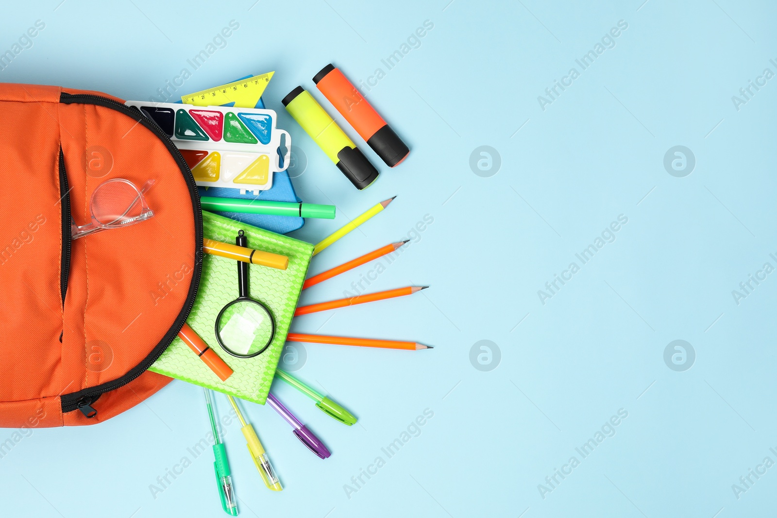 Photo of Orange backpack and different school supplies on light blue background, flat lay. Space for text