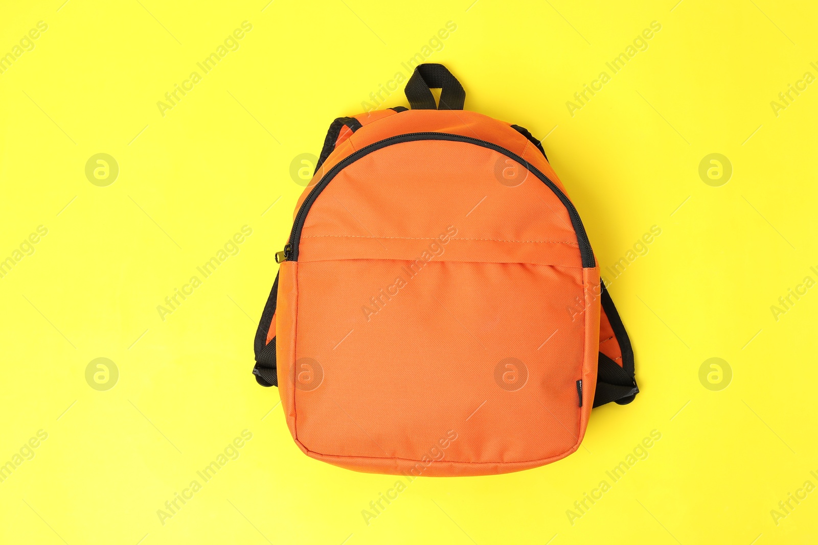 Photo of One orange backpack on yellow background, top view. Back to school