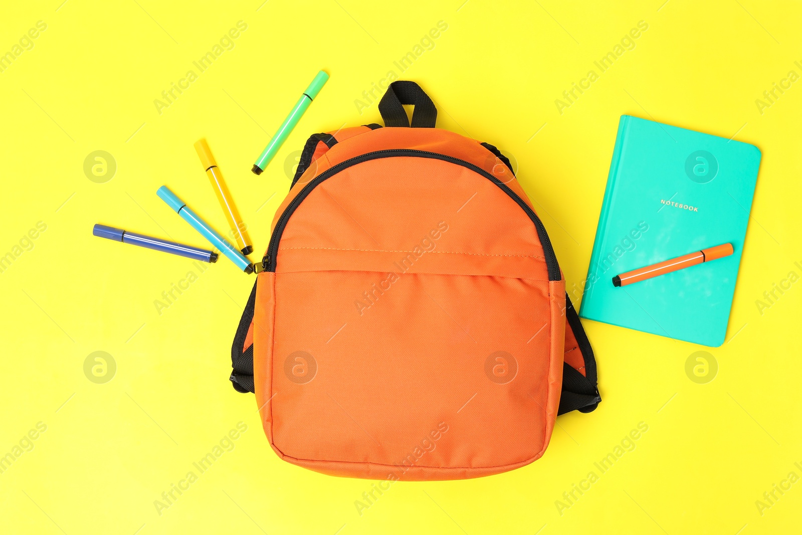 Photo of Orange backpack, felt pens and notebook on yellow background, flat lay