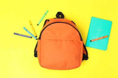 Photo of Orange backpack, felt pens and notebook on yellow background, flat lay