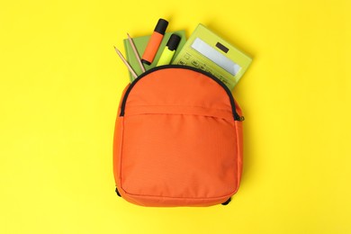 Photo of Orange backpack with different school supplies on yellow background, top view