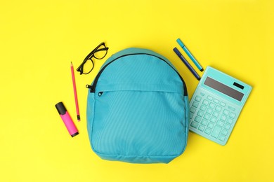 Photo of Light blue backpack and different school supplies on yellow background, flat lay