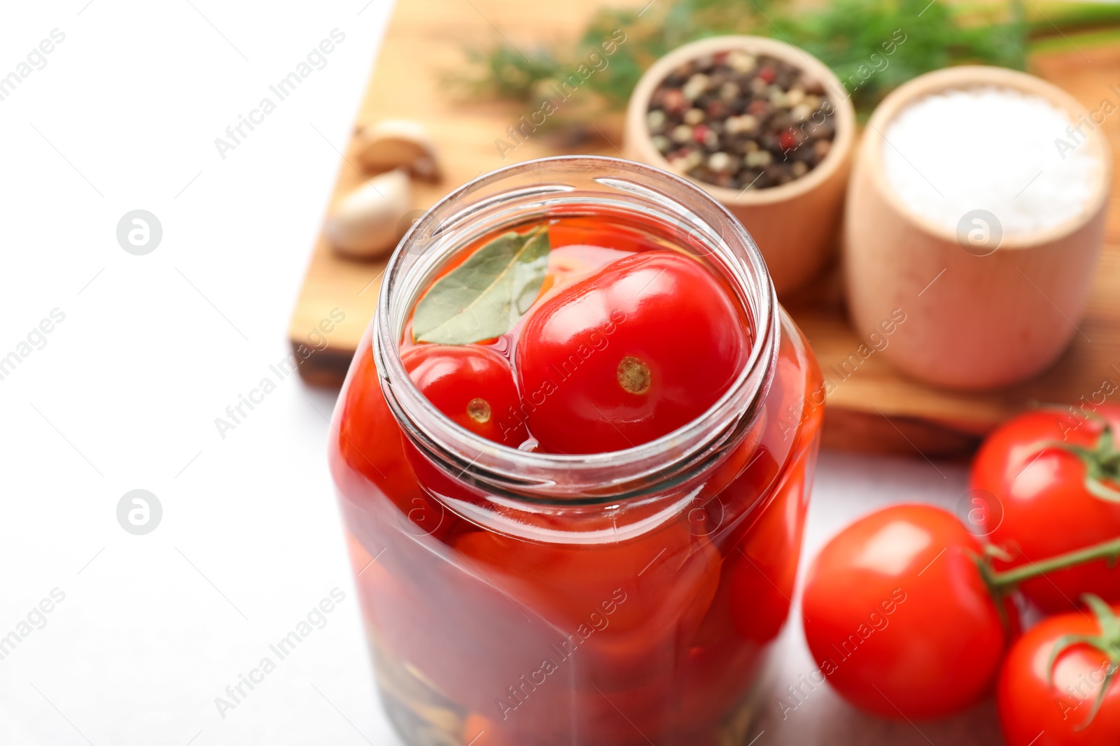 Photo of Tasty pickled tomatoes in jar, fresh vegetables and spices on white table, closeup