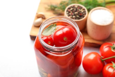 Photo of Tasty pickled tomatoes in jar, fresh vegetables and spices on white table, closeup