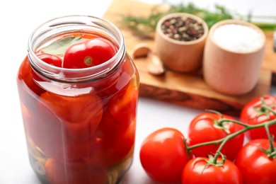 Photo of Tasty pickled tomatoes in jar, fresh vegetables and spices on white table, closeup