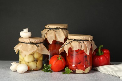 Photo of Different pickled products in jars and fresh ingredients on grey table