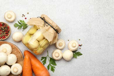 Photo of Tasty pickled mushrooms in jar and fresh ingredients on grey table, flat lay. Space for text