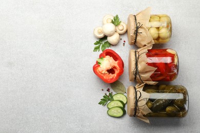 Photo of Different pickled products in jars and fresh ingredients on grey table, flat lay. Space for text