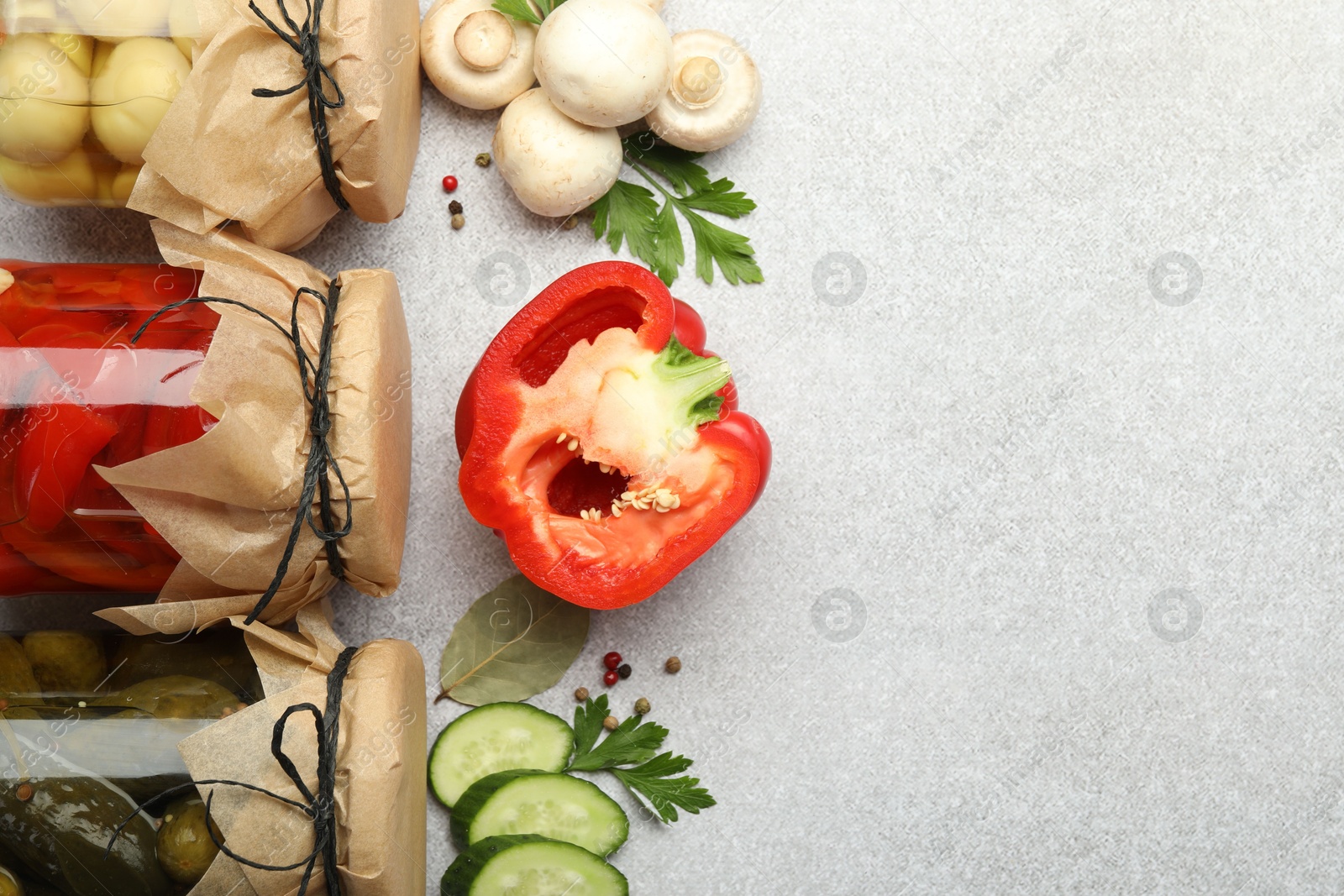 Photo of Different pickled products in jars and fresh ingredients on grey table, flat lay. Space for text