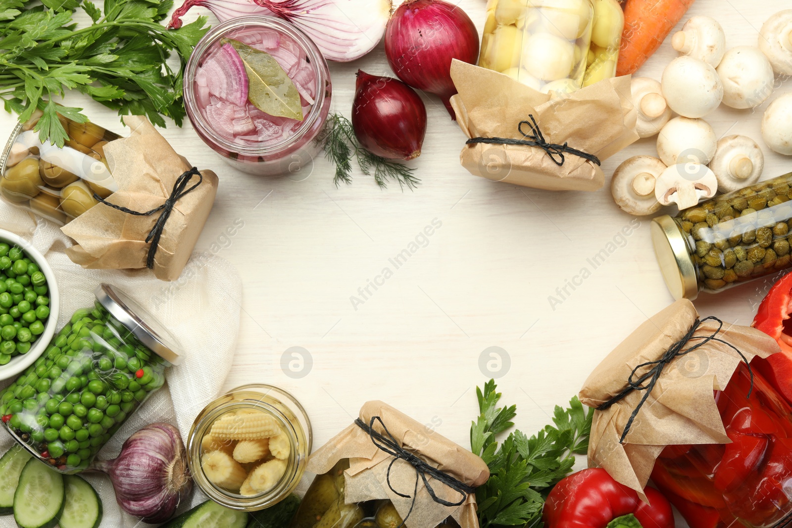 Photo of Different pickled products in jars and fresh ingredients on white wooden table, flat lay. Space for text