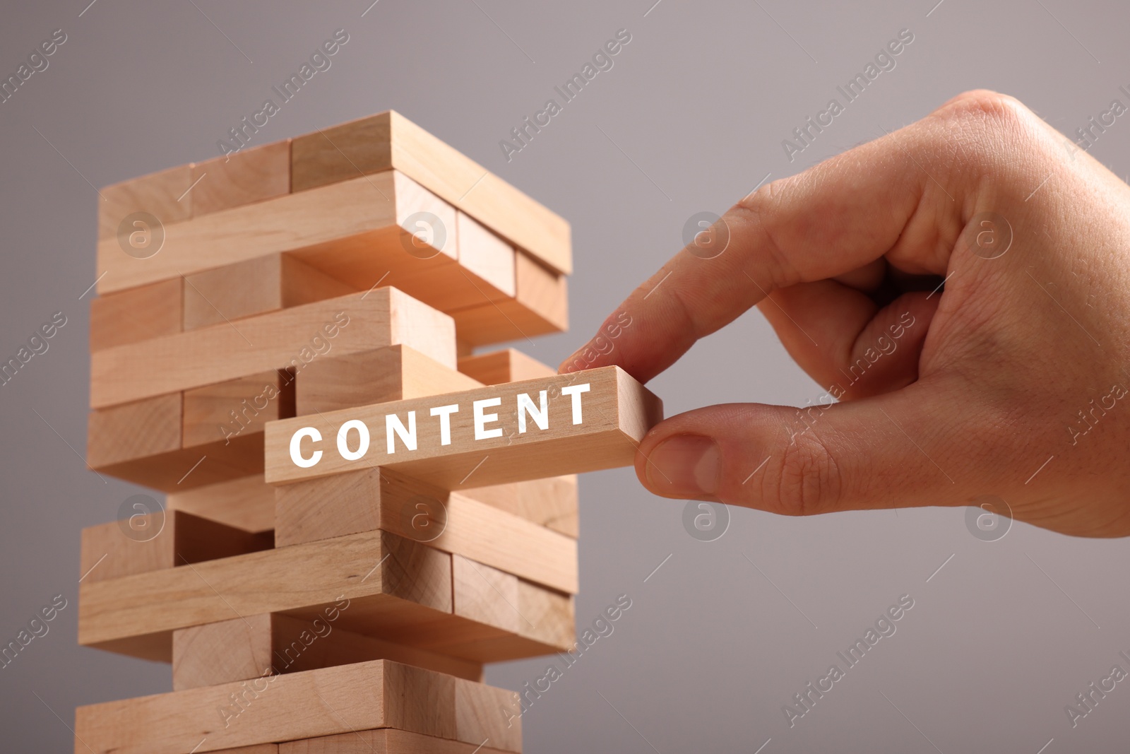 Image of Man removing wooden block with Content from tower on grey background, closeup