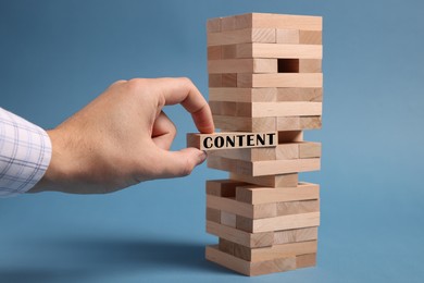 Image of Man removing wooden block with Content from tower on light blue background, closeup