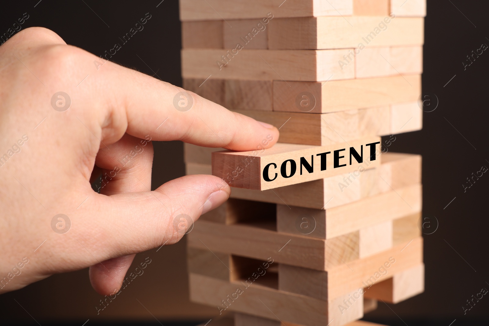 Image of Man removing wooden block with Content from tower on dark background, closeup