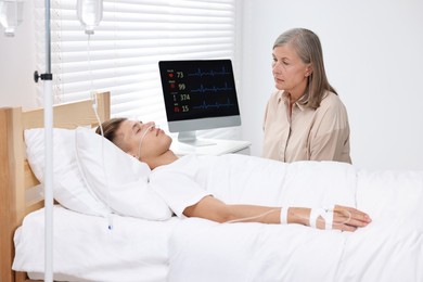 Photo of Coma patient. Sad mature woman near her unconscious son in hospital