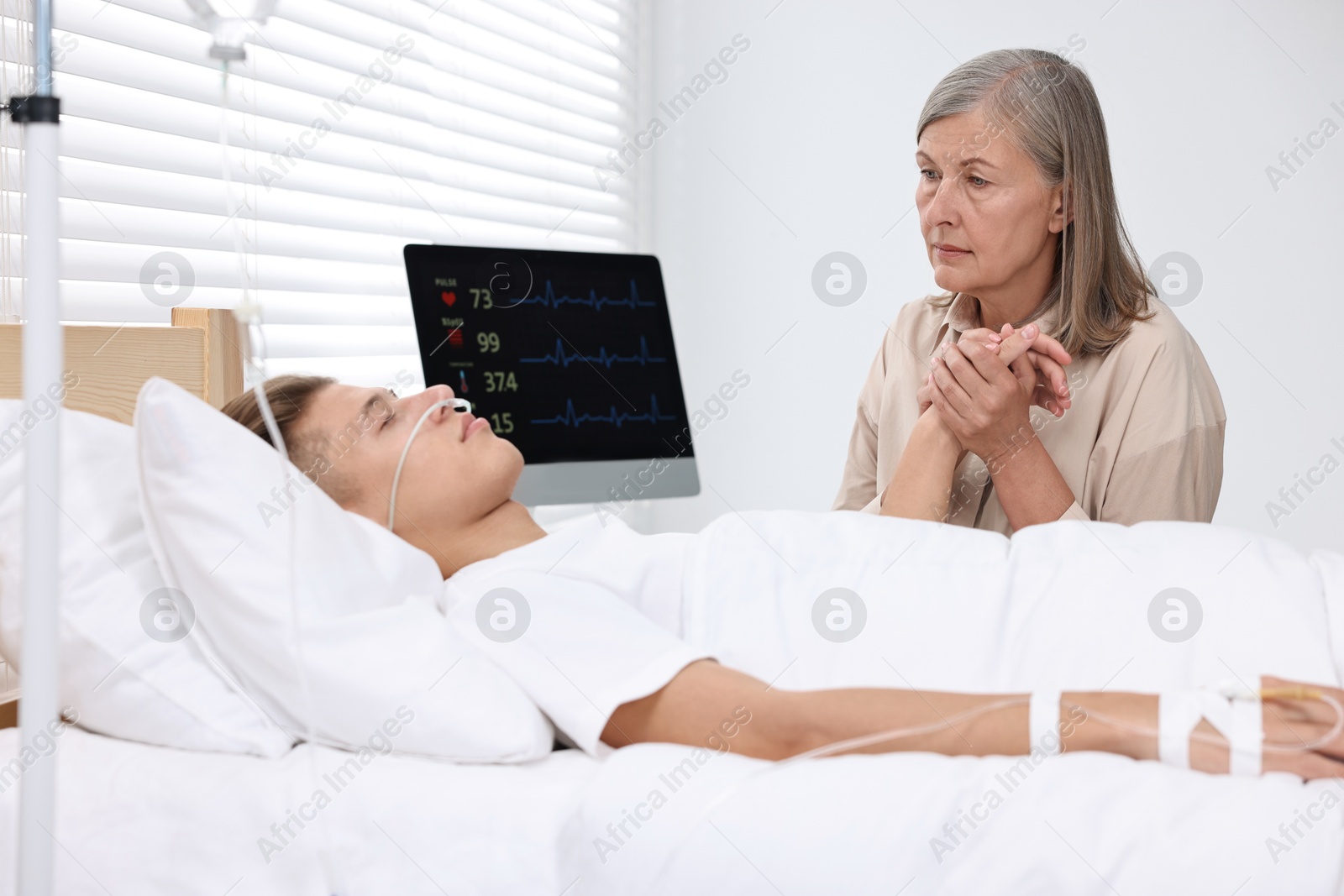 Photo of Coma patient. Sad mature woman near her unconscious son in hospital