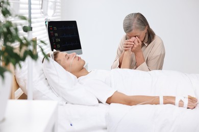 Photo of Coma patient. Sad mature woman near her unconscious son in hospital