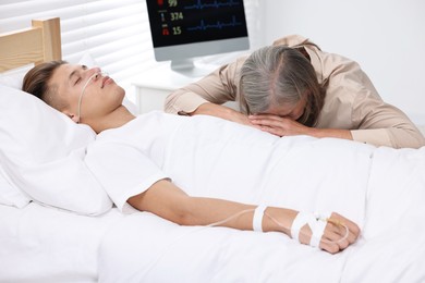 Photo of Coma patient. Sad mature woman near her unconscious son in hospital