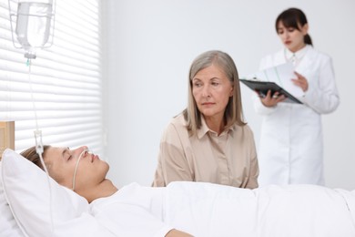 Photo of Coma patient. Sad mature woman near her unconscious son in hospital