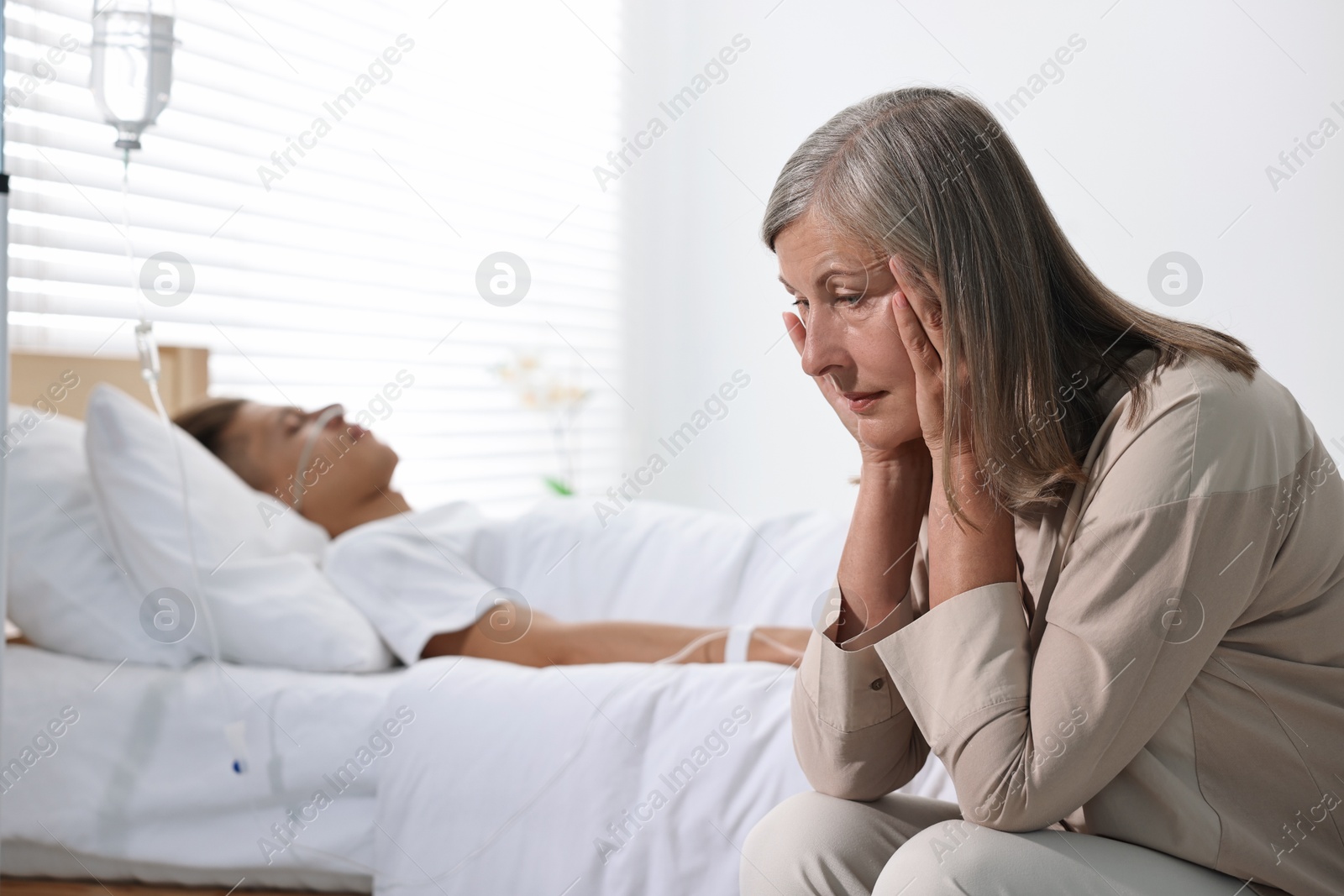 Photo of Coma patient. Sad mature woman near her unconscious son in hospital