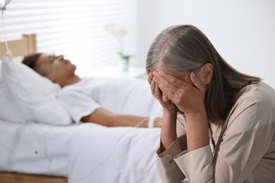 Photo of Coma patient. Sad mature woman near her unconscious son in hospital