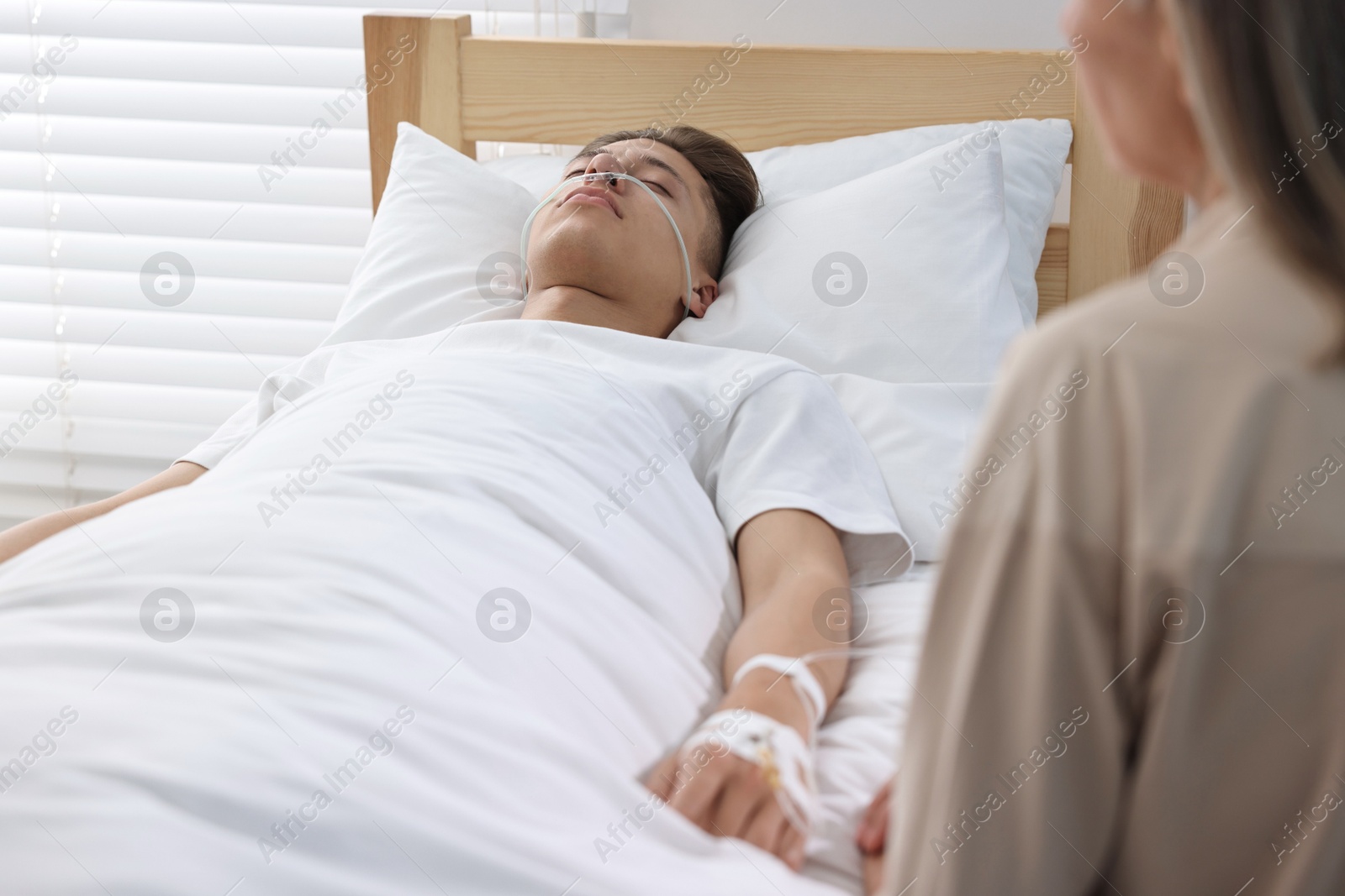 Photo of Coma patient. Sad mature woman near her unconscious son in hospital