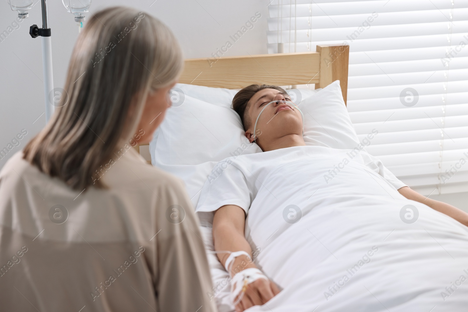 Photo of Coma patient. Sad mature woman near her unconscious son in hospital