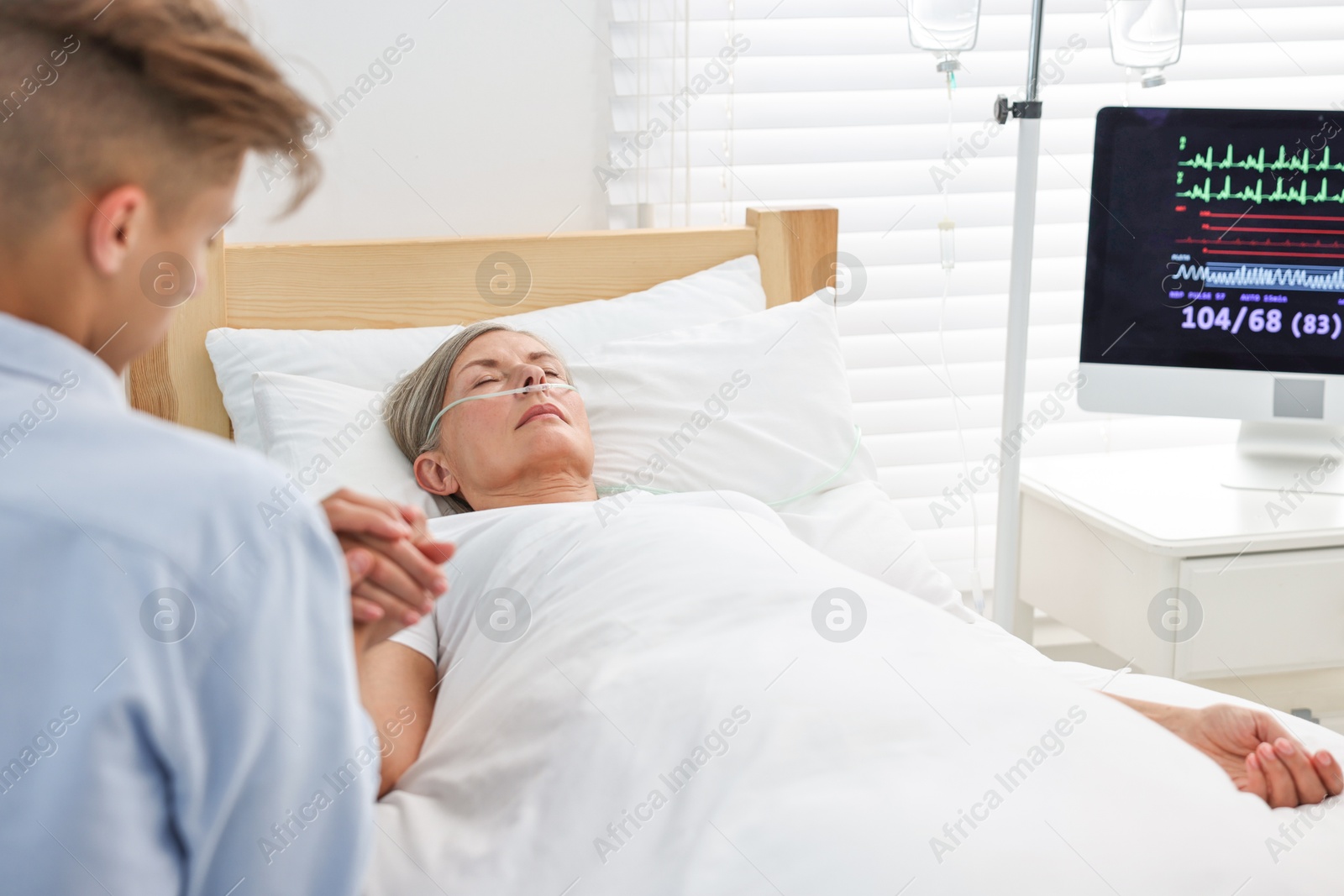 Photo of Coma patient. Man near his unconscious mother in hospital