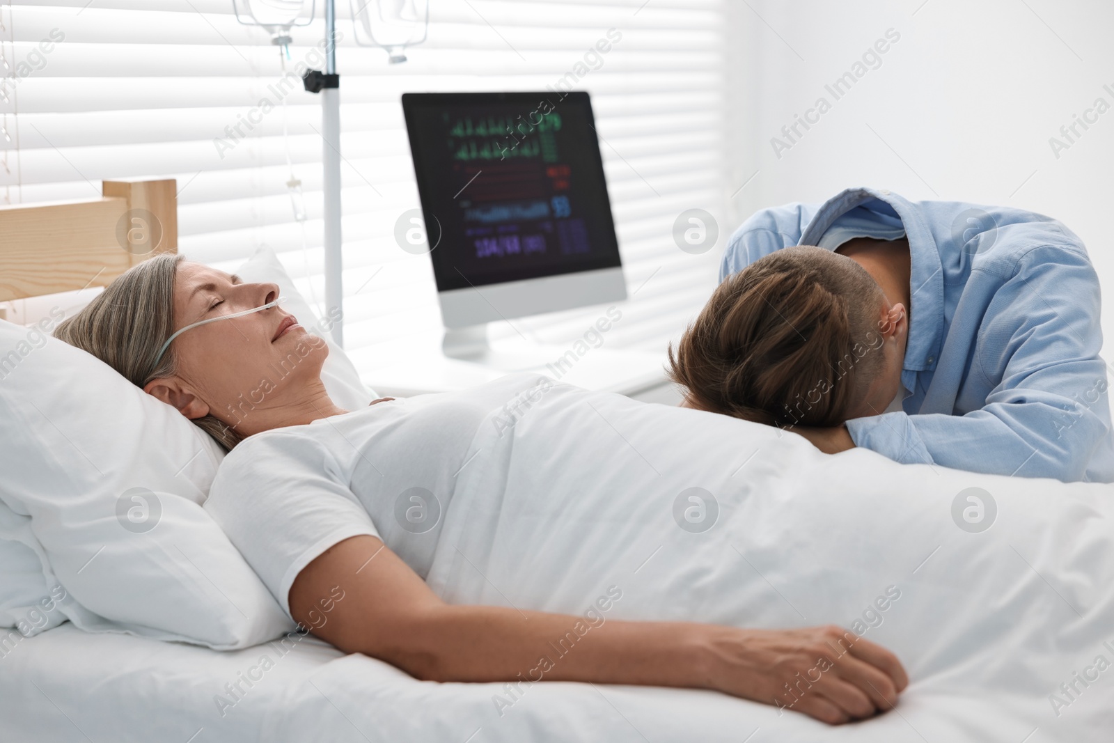 Photo of Coma patient. Sad young man near his unconscious mother in hospital