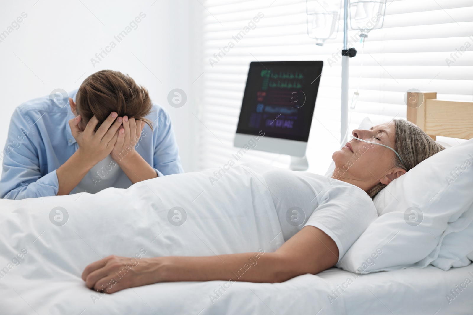 Photo of Coma patient. Sad young man near his unconscious mother in hospital