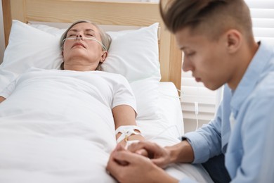 Photo of Coma patient. Sad young man near his unconscious mother in hospital