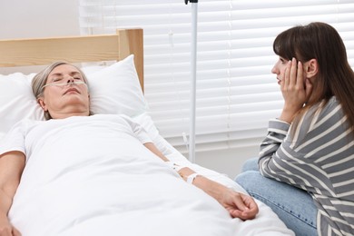 Photo of Coma patient. Sad young woman near her unconscious mother in hospital