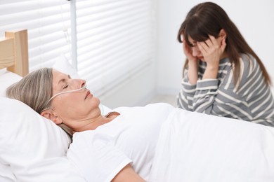 Photo of Coma patient. Sad young woman near her unconscious mother in hospital