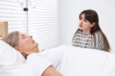 Photo of Coma patient. Sad young woman near her unconscious mother in hospital