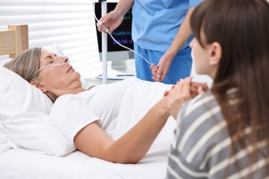 Coma patient. Sad young woman near her unconscious mother in hospital