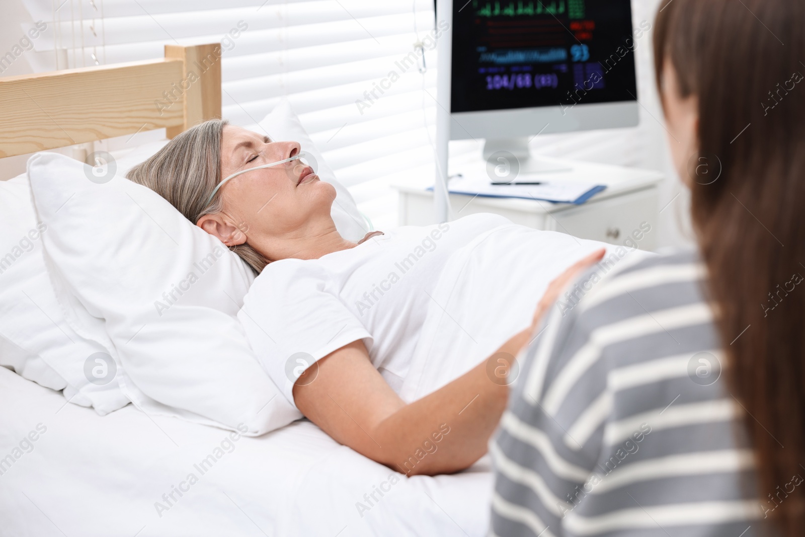 Photo of Coma patient. Woman near her unconscious mother in hospital