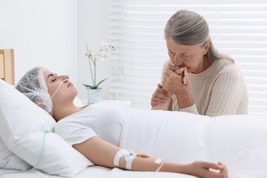 Photo of Coma patient. Sad mature woman near her unconscious daughter in hospital