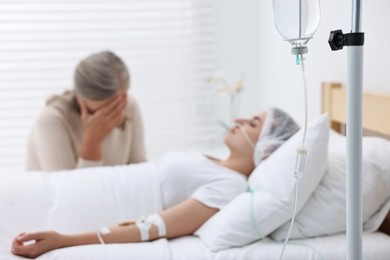 Coma patient. Sad mature woman near her unconscious daughter in hospital, selective focus