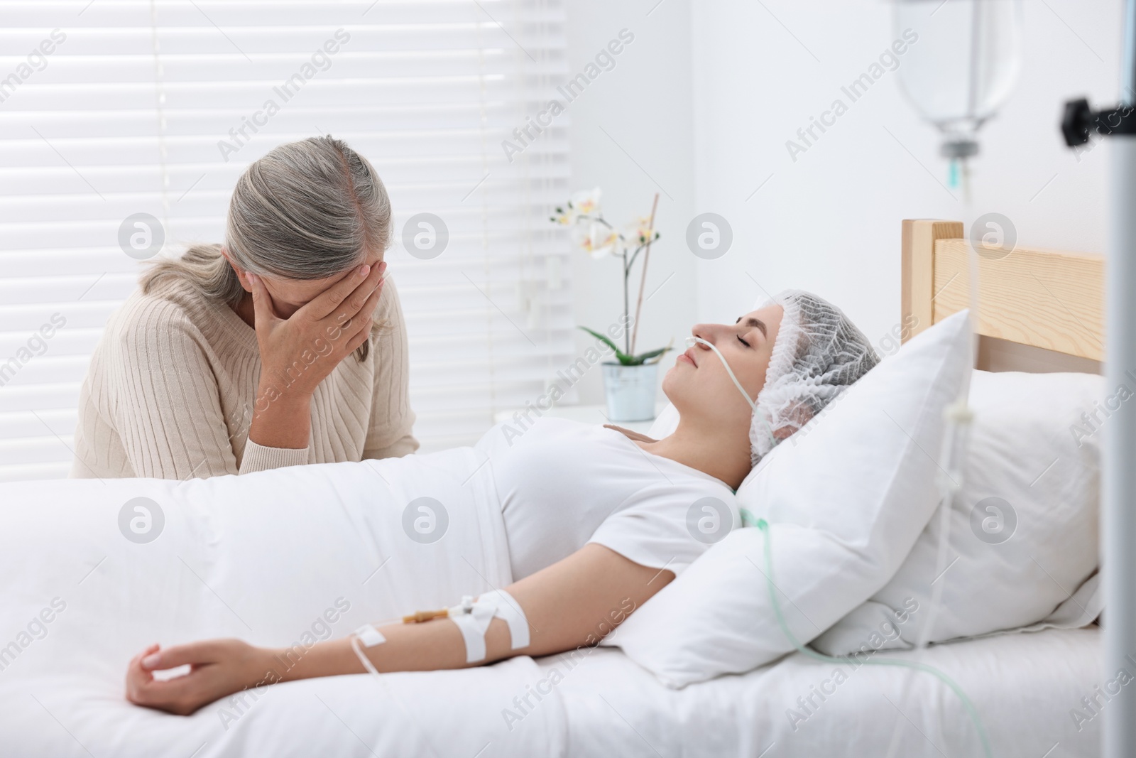 Photo of Coma patient. Sad mature woman near her unconscious daughter in hospital