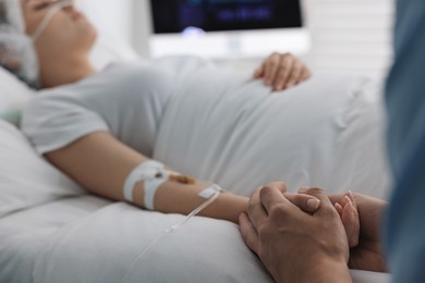 Coma patient. Man near his unconscious wife in hospital, selective focus