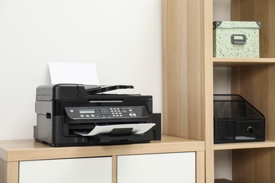 Photo of Modern printer with paper on wooden nightstand in office